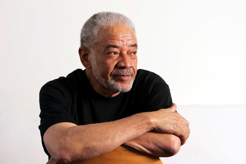 A man sits backwards on a chair, leaning on his arms folded on top of the back rest.