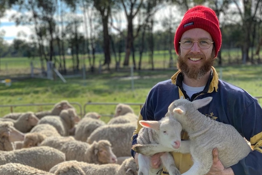 A man in a beanie cuddling lambs.