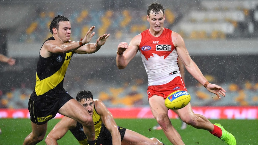 Jordan Dawson kicks a yellow ball past Daniel Rioli, who is approaching from Dawson's right with his arms raised