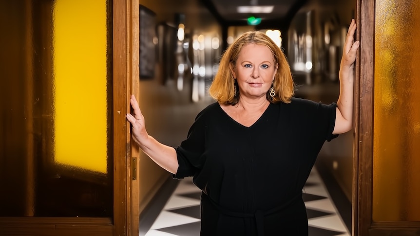 Suzanne Chaundy stands in the entrance of a tiled corridor with her hands on the doorframe.