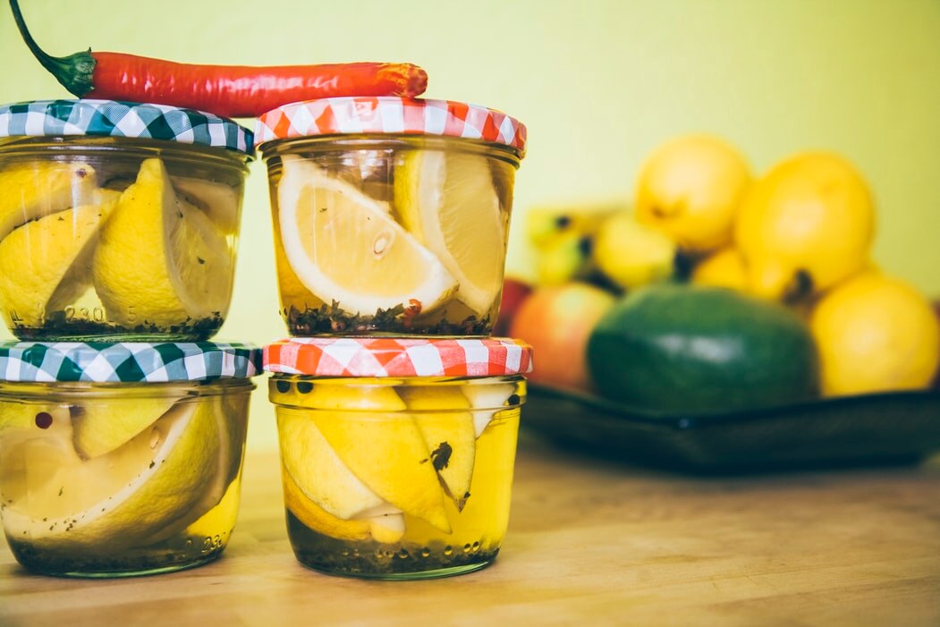 Small jars of lemon slices pickling on bench with a chili on the top for a story about pickling tips.
