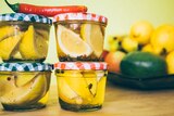 Small jars of lemon slices pickling on bench with a chili on the top for a story about pickling tips.
