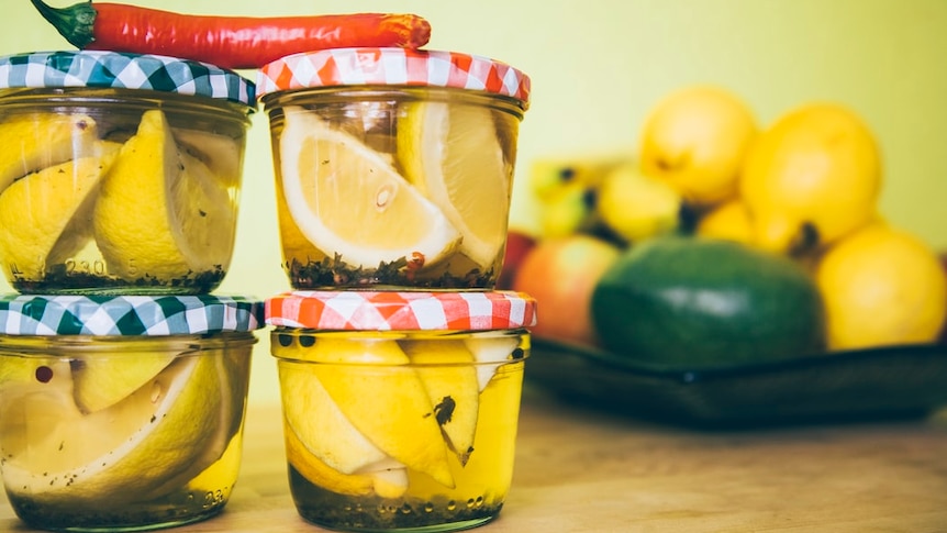 Small jars of lemon slices pickling on bench with a chili on top of them for a story about pickling tips.