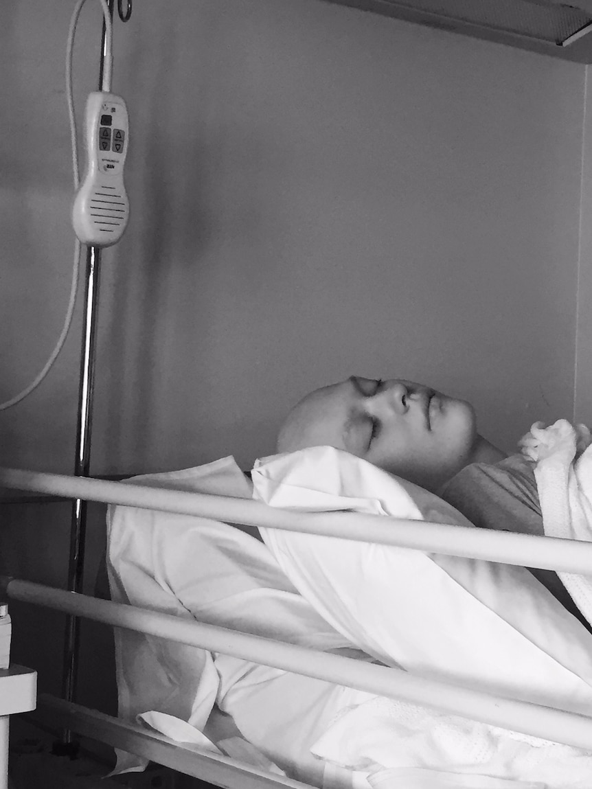 a teenage girl sleeps in a hospital bed, she is bald from cancer treatment. 