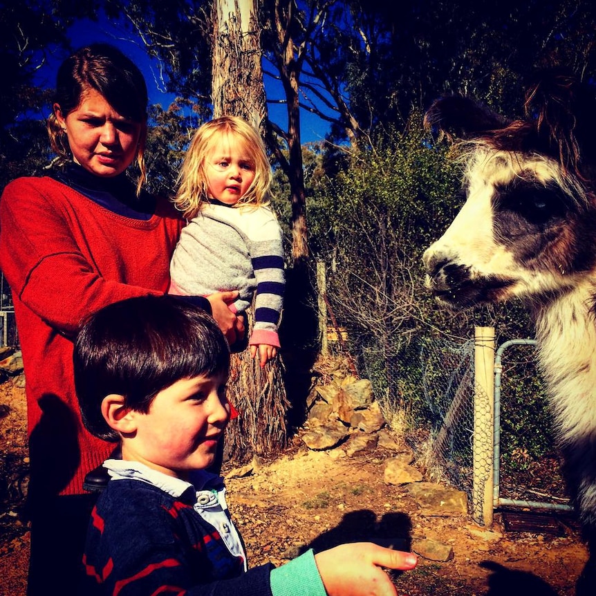 Babysitter Chloe Mackenzie with two kids standing next to a goat