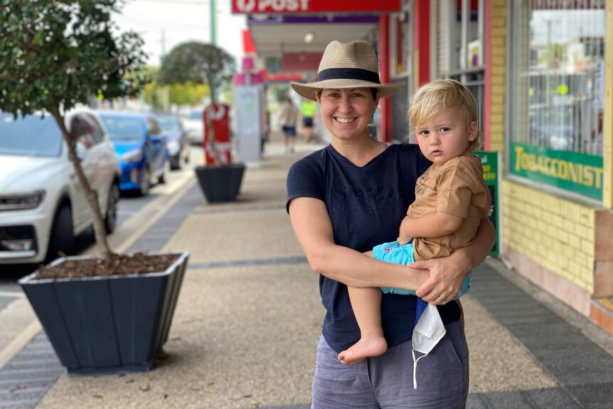 Smiling woman standing on a footpath holding a male toddler.