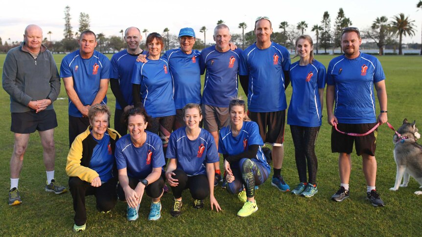 A group of men and women in blue running shirts and gear pose for a photo at Langley Park.