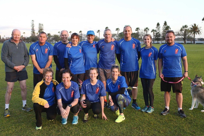A group of men and women in blue running shirts and gear pose for a photo at Langley Park.