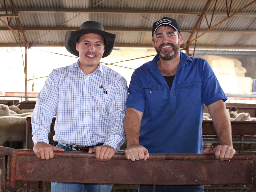 Two men, Lincoln McKinlay and Scott Mitchell, standing in a shed leaning on a fence facing the camera and smiling.