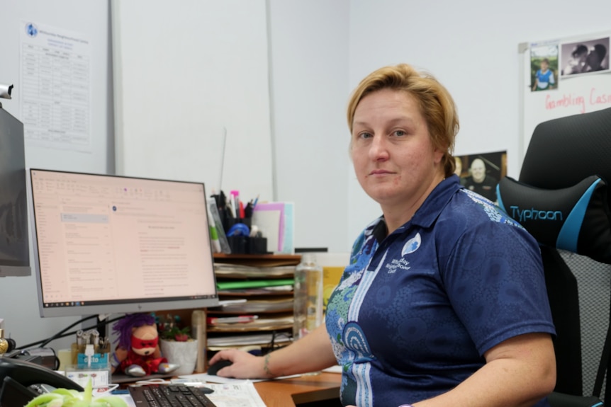 a woman sits in an office behind a desk with a hand on the mouse and looking at the camera