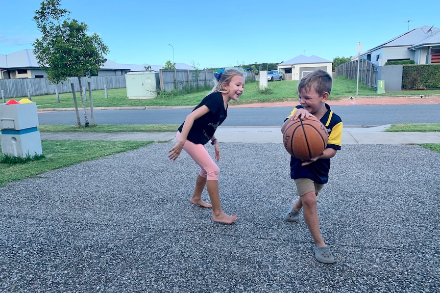 a girl and a boy playing basketball on a driveway