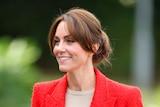 A close up of the princess smiling. She wears a bright red blazer and her brown hair is in a low bun