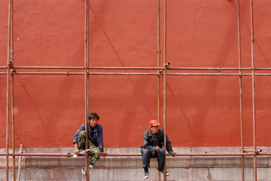 Los trabajadores se sientan en un andamio en un sitio de construcción en la Ciudad Prohibida en Beijing.