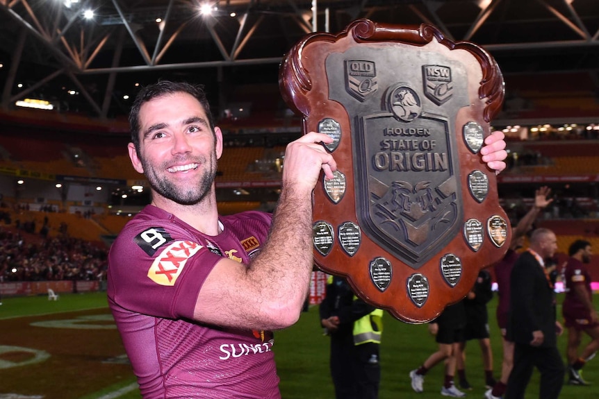 Cameron Smith smiling as he holds aloft the State of Origin winners shield in 2015.