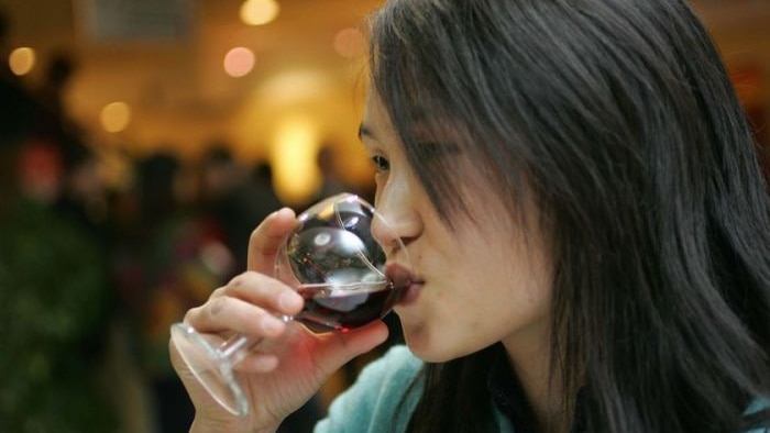 Woman with dark hair drinking red wine out of a glass at a bar.