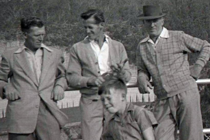 Three men leaning against a fence with a young boy in the front.
