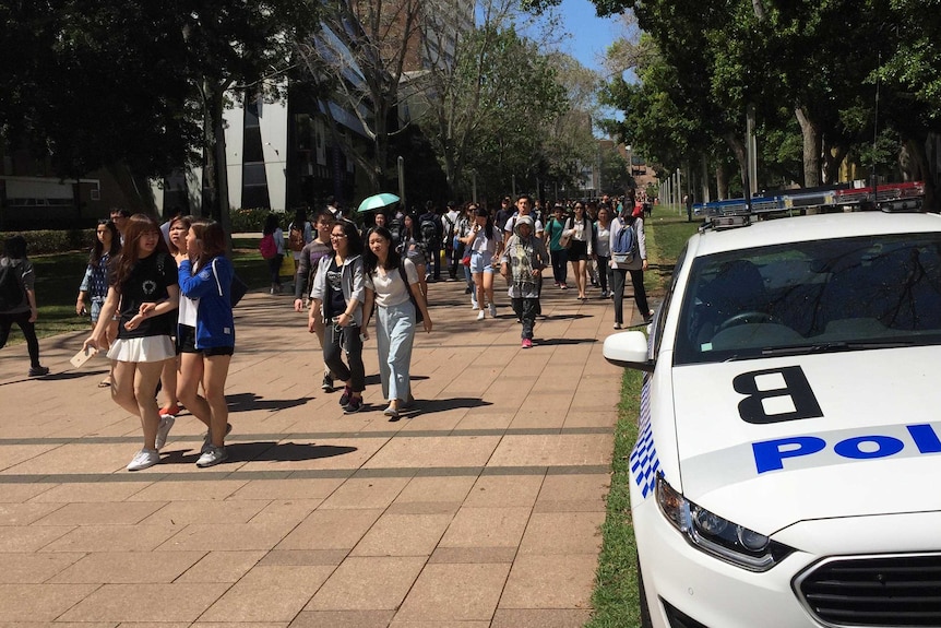 Students at UNSW walk past a police car on the campus after threats were made on social media against staff and students.