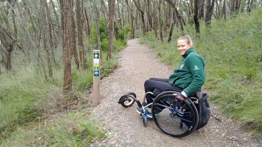 A smiling Yvette Eglinton riding along a walking trail in a wheelchair. 