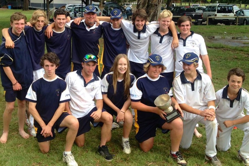 Lauren Cheatle and an all-boys under 16's cricket team gather for a photo with a large trophy.