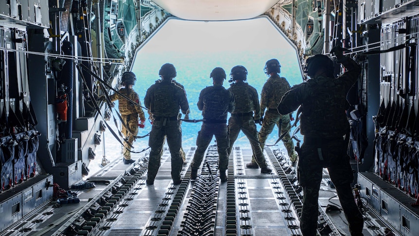Men in combat gear stand at the mouth of an open plane