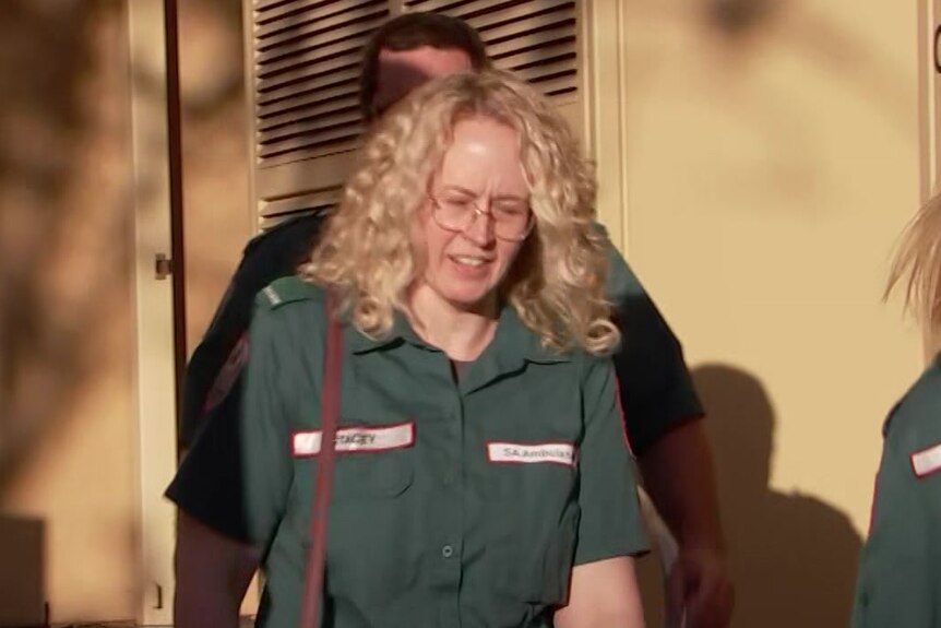 Blonde, curly-haired woman wearing glasses and a green paramedic uniform outside a sandstone court building
