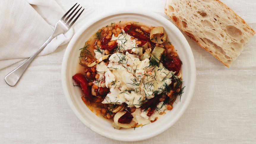 A bowl of slow-roasted tomatoes and fennel topped with baked fish and a creme fraiche sauce, a cold weather meal.