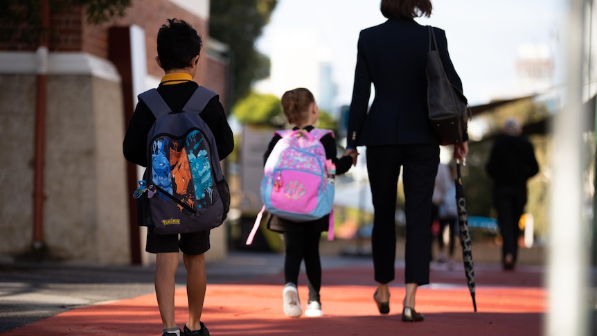Boy walks into school behind a girl holding her mum's hand.