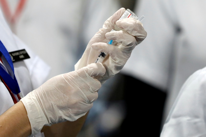 A worker wearing gloves fills a syringe with a coronavirus vaccine