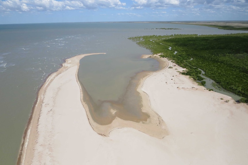 A photo taken from the air of a beach point meeting the ocean with wetlands to the side.