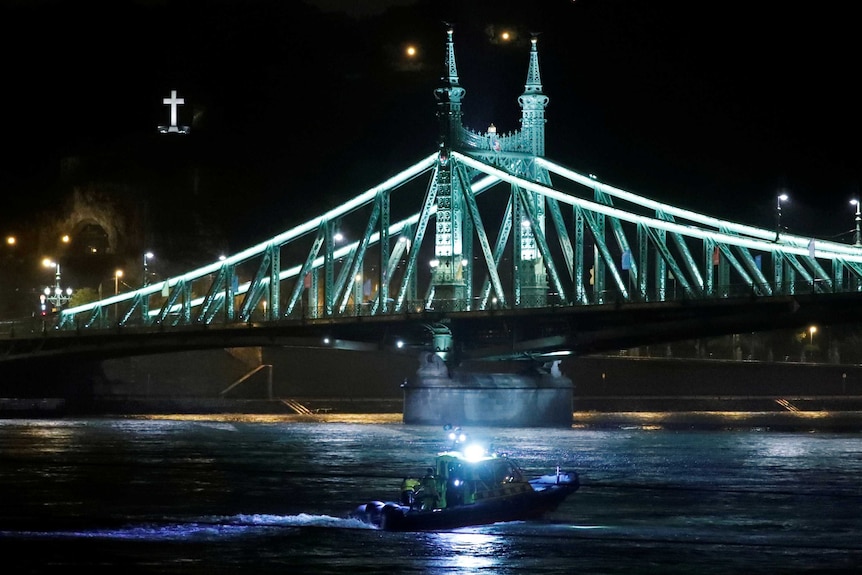 A rescue boat sails in front of a large illuminated bridge.