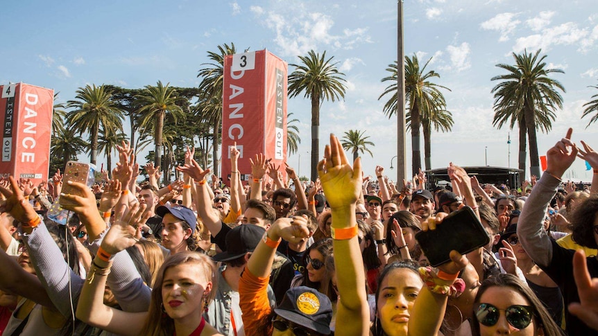 Crowd with hands up in front of red Listen Out branded pillars that read 'DANCE' and palm trees.
