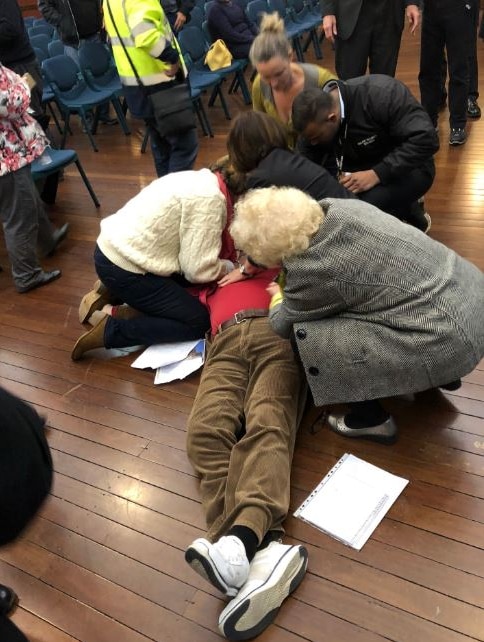 A group of people attend to a man laying on a hard wood floor.