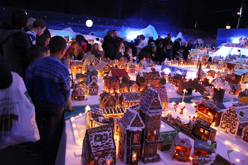 Adults and kids look at a large model town made from gingerbread.