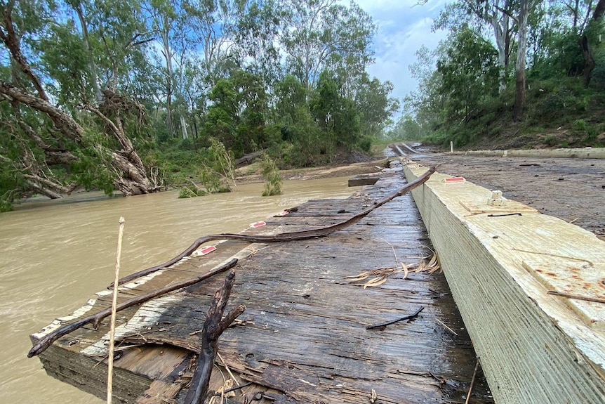 A damaged bridge with flooded creek water just below road level