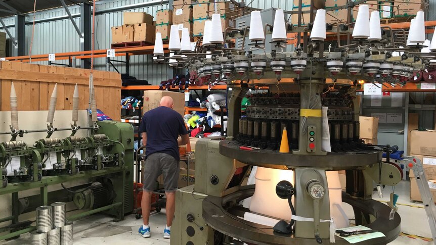 Man stands in front of machine that is spinning wool.