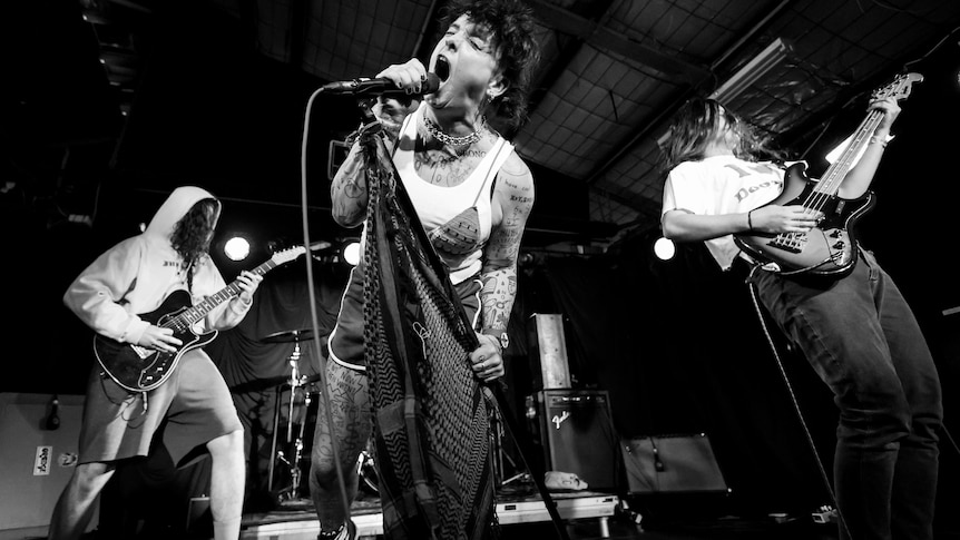 Black and white photo of a punk band. The lead singer is screaming into the mic.