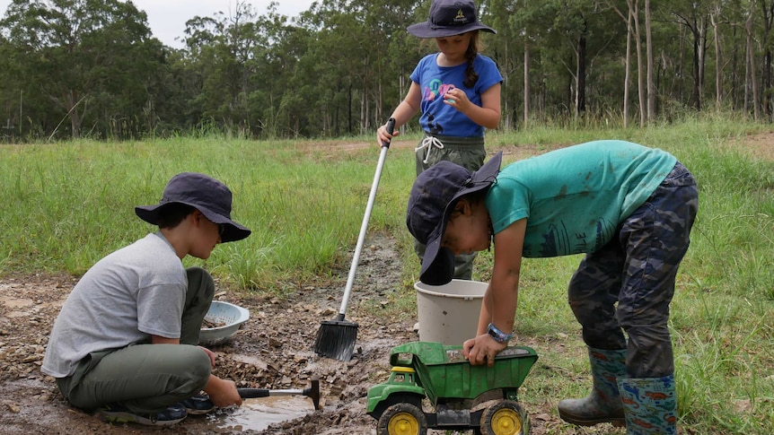 Two boys and a girl dig and play in the mud and dirt.