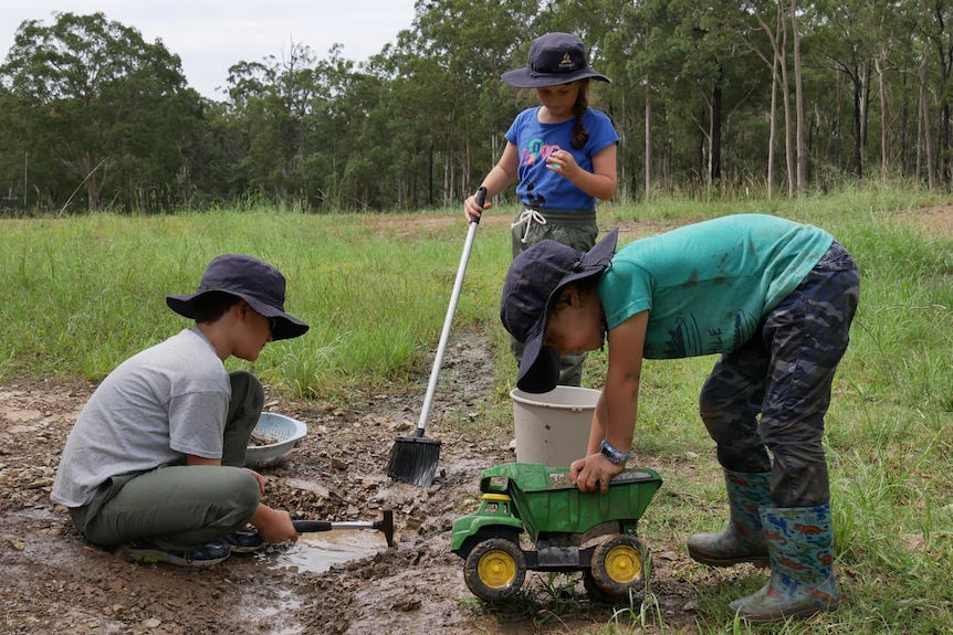 Two boys and a girl dig and play in the mud and dirt.