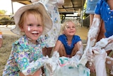 Two little girls smile as they play with a bucket of foam, which has gotten all up their arms.