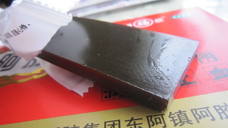 A dark red slab of ejiao half unwrapped lying on a box.