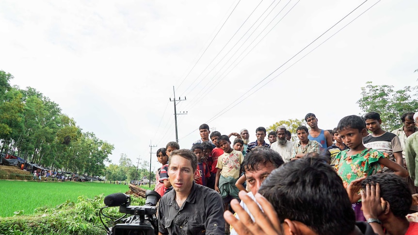 James Bennett films in Bangladesh with a crowd of Rohingya refugees standing behind him