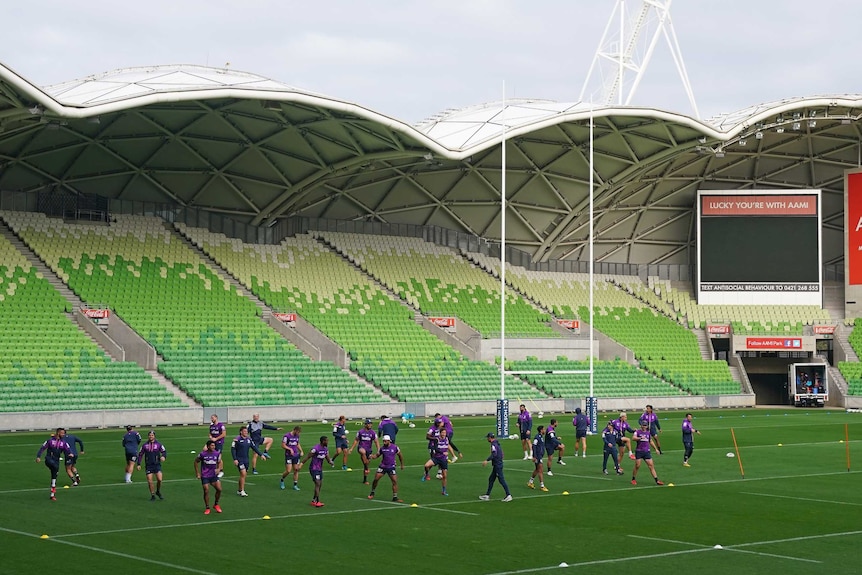 A group of players run on the park at training, with the goalposts and grandstand in the background.