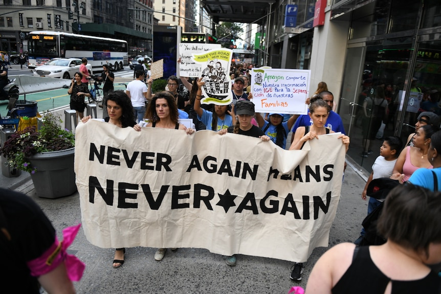 Four women carrying a banner that says 'never again means never again'.