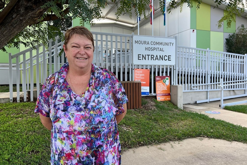 A woman stands in front of the Moura Hospital and smiles at the camera.