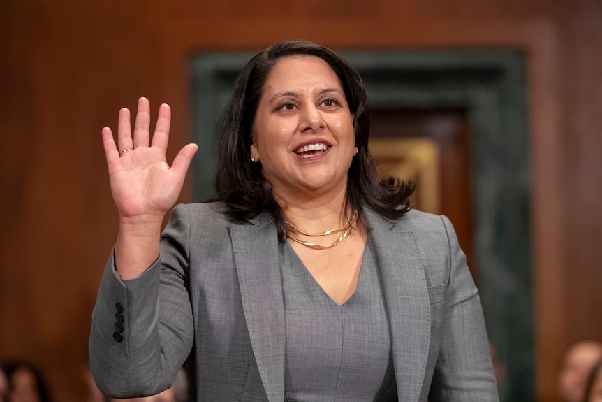 A woman in a grey blazer smiling as she raises her hand to take an oath.