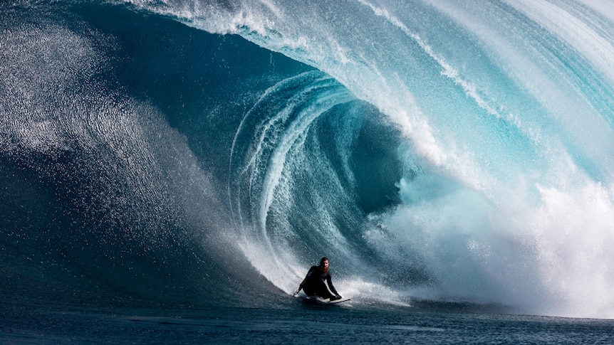 A surfer crouching down at the base of a huge wave.