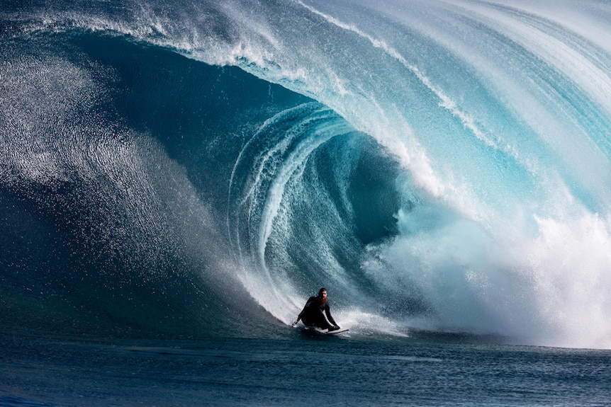 A surfer crouching down at the base of a huge wave.