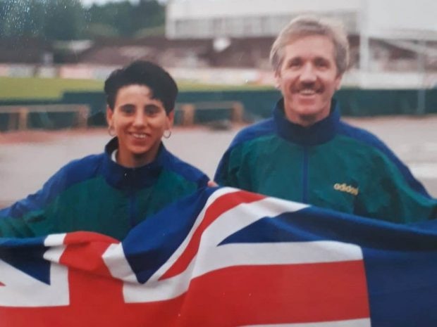 A woman and a man wearing matching blue and green jackets hold an Australian flag and smile