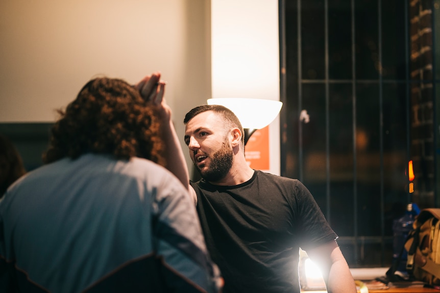 A young man with close-cropped dark hair gives another man a haircut