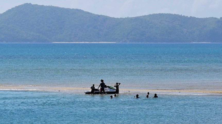 A boat and children in the water with another island in the background